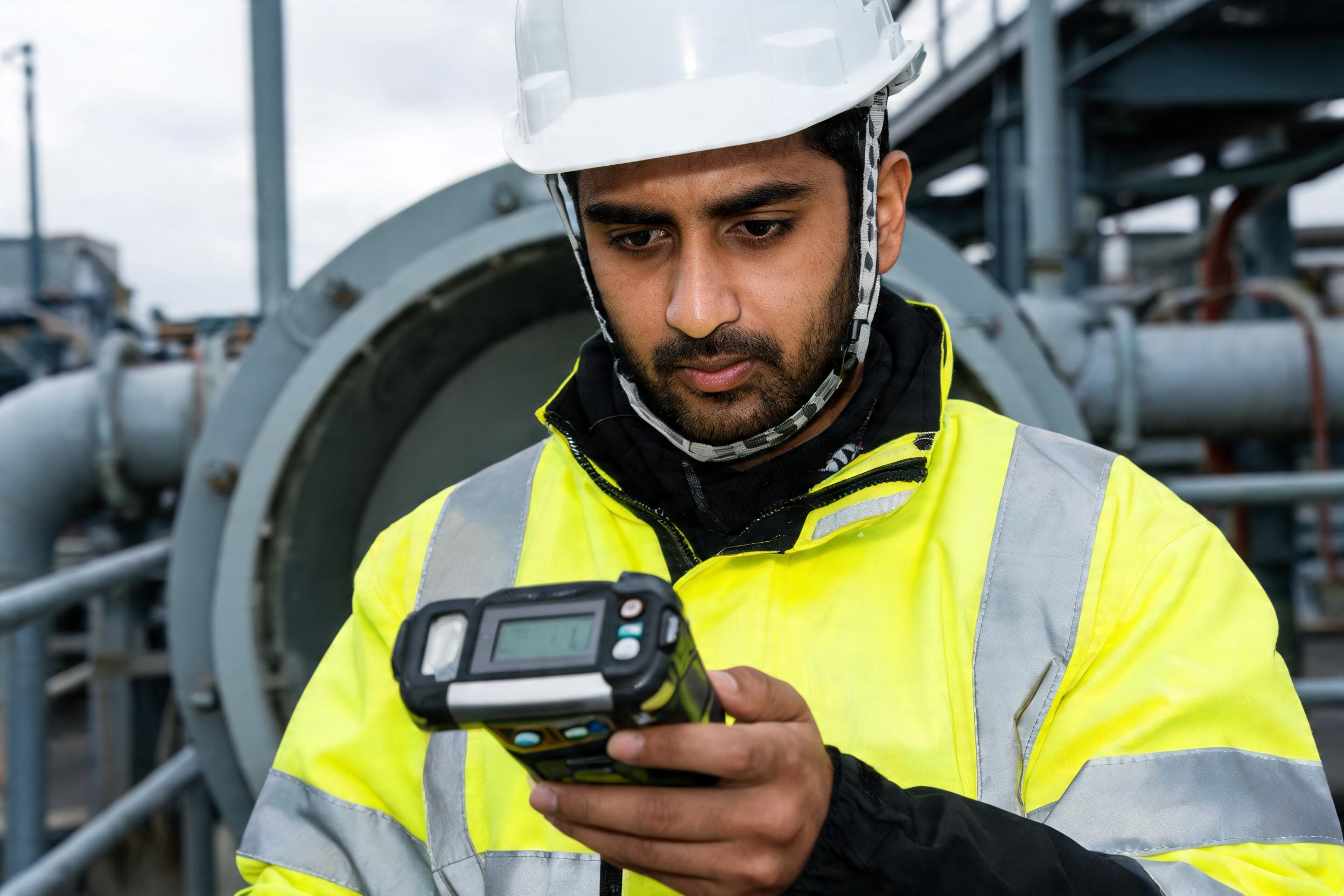 Worker checking a handheld gas detector before a confined-space entry