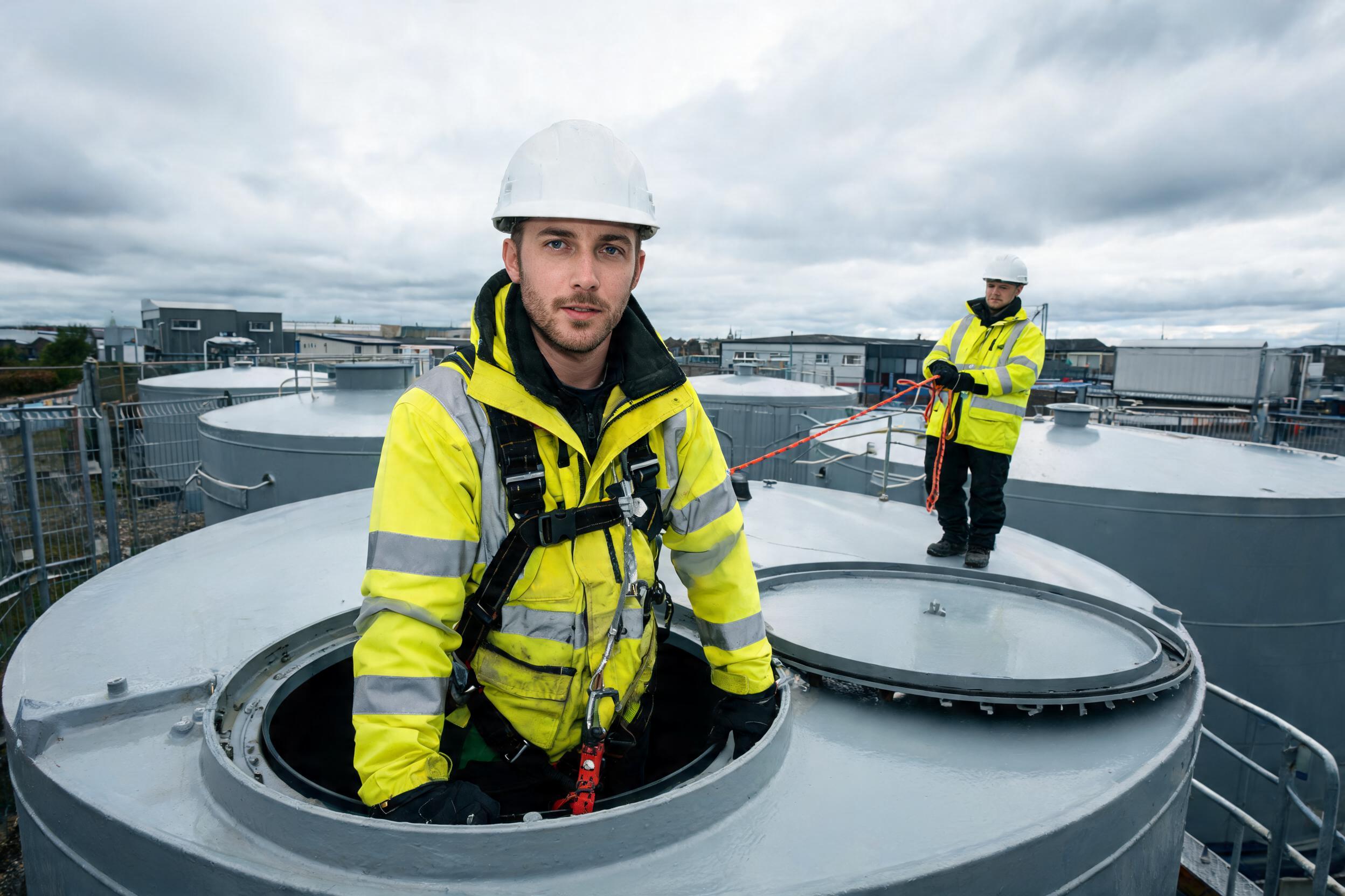 Worker entering a storage tank with an attendant holding the safety line