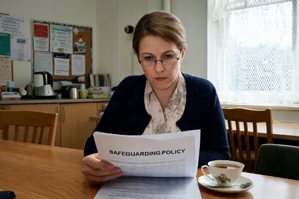 Teacher reading a school safeguarding policy document in the staff room