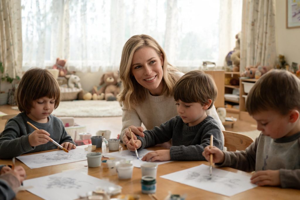 Nursery practitioner helping children with a painting activity